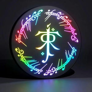 May include: A round, black decorative item with a glowing, multi-colored design. The design features a central symbol and surrounding text in a stylized font, with a rainbow gradient effect. The letters "RGB" are in the bottom right corner.