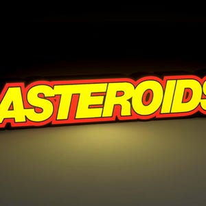 Puede incluir: La palabra "ASTEROIDS" en letras amarillas con contorno rojo, sobre un fondo oscuro. Las letras parecen ser 3D, con un ligero efecto de sombra, dándoles una apariencia en relieve.