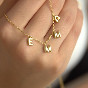 May include: A gold chain necklace with a charm of the letter 'E' and two charms of the letter 'M'.