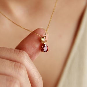 May include: A gold chain necklace with a teardrop-shaped red gemstone pendant and a smaller yellow gemstone accent.