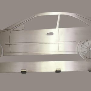 Puede incluir: Un llavero de metal plateado con forma de coche. El llavero es un perfil lateral de un cupé con alerón y cinco ganchos para llaves debajo. El coche tiene ruedas y ventanas detalladas. El llavero está montado sobre un fondo gris.