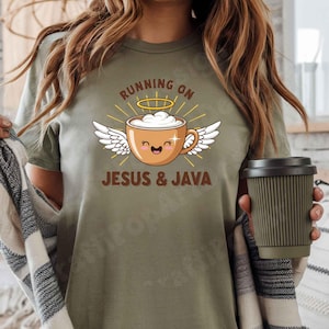 May include: Olive green t-shirt with the text "RUNNING ON JESUS & JAVA". The graphic features a smiling coffee cup with angel wings and a halo. A reusable coffee cup is held in the hand.