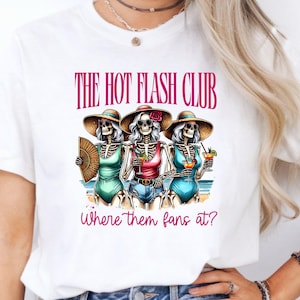 May include: White t-shirt featuring a graphic of three skeleton figures on a beach, wearing swimsuits and sun hats, holding drinks and a fan. The text "THE HOT FLASH CLUB" and "where them fans at?" are printed above and below the graphic.