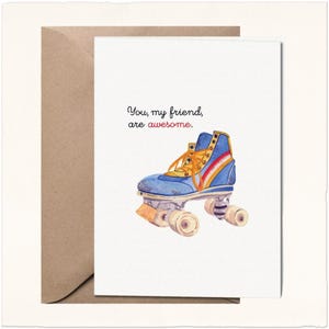 May include: A white greeting card featuring a watercolor illustration of a blue roller skate with orange laces and a red and white side stripe. The text above the skate reads, "You, my friend, are awesome." The card is paired with a brown envelope.