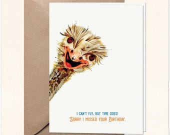 Puede incluir: Una tarjeta de felicitación blanca con una ilustración en acuarela de una cabeza de avestruz asomándose por el lado izquierdo. El texto dice: I CAN'T FLY, BUT TIME DOES! SORRY I MISSED YOUR BIRTHDAY. La tarjeta está sobre un sobre de papel marrón.