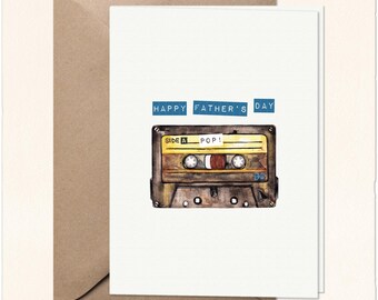 May include: A white greeting card featuring a watercolour illustration of a brown and yellow cassette tape with the text "SIDE A POP!" on the label. Above the cassette, the text "HAPPY FATHER'S DAY" is printed in blue rectangular boxes.