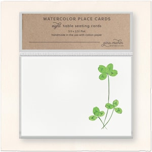 May include: Watercolor place cards with a four-leaf clover design. The cards are 3.5 x 2.5 inches and handmade in the USA with cotton paper. The top of the cards reads "WATERCOLOR PLACE CARDS" and "eight table seating cards."