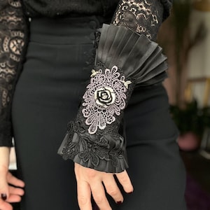 May include: Black lace cuff with a pleated satin ruffle and a black rose embellishment.