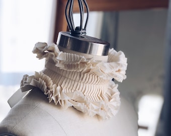 May include: A white ruffled collar on a dress form. The collar is made of a soft, delicate fabric and has a vintage look.