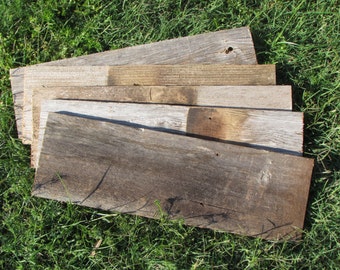 May include: A stack of five weathered wooden boards, showing different shades of brown and gray. The boards are arranged in a fan shape, with the longest board at the bottom.
