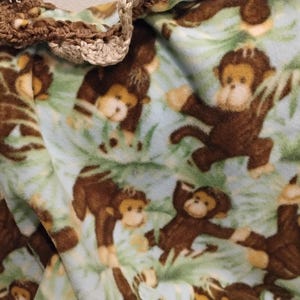 May include: A blue and green fleece blanket with a brown monkey pattern. The blanket has a crocheted border.