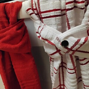 May include: Two kitchen towels hanging on a rack. One towel is red and the other is white with red stripes. Both towels have a metal button on them.