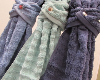 May include: Three towels hanging on a rack, one is blue, one is light blue, and one is dark blue. Each towel has a button closure.