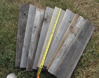 May include: A collection of five weathered wooden planks, some with knots and nail holes, arranged in a fan shape. A yellow measuring tape is used to measure the length of the planks, which are approximately 18 inches long.