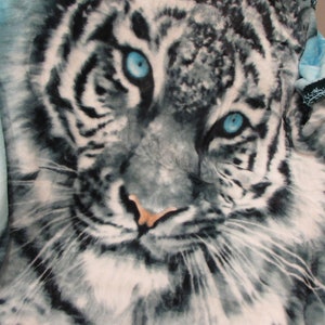 May include: A white and blue fleece blanket with a white tiger face printed on it. The tiger has blue eyes and a pink nose.