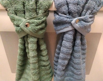 May include: Two kitchen towels hanging on a metal oven door handle. The towel on the left is green and the towel on the right is blue. Both towels are tied in a knot and secured with a metal button.
