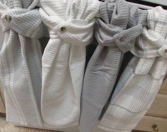 May include: Four kitchen towels hanging on a rack. Two towels are white with a waffle texture and two towels are gray with a waffle texture. The towels have a button on the top to hold them in place.