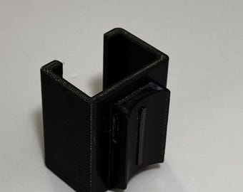 May include: A black, 3D-printed plastic clip, designed to hold an object. The clip has a rectangular shape with a U-shaped opening and a smaller rectangular piece attached to the side. The clip is made of a textured material.