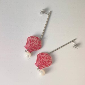 Peut inclure: Boucles d'oreilles pendantes avec un motif de coquillage rouge et blanc et un accent de perle. Les boucles d'oreilles ont une tige droite de couleur argentée. Le motif de coquillage a un motif en forme d'éventail.