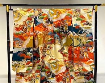 May include: A vibrant Japanese kimono with a colorful pattern of cranes, carts, and foliage. The kimono features a rich palette of orange, gold, blue, and green. It is displayed on a black stand, showcasing its intricate design and cultural significance.