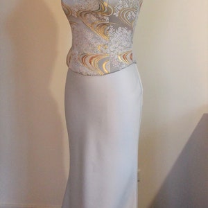 Puede incluir: Un vestido de novia sin tirantes con una falda de sat&eacute;n blanco y un corpi&ntilde;o con un estampado floral blanco y dorado.