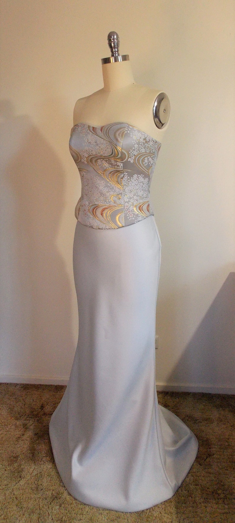 Puede incluir: Un vestido de novia sin tirantes con una falda de sat&eacute;n blanco y un corpi&ntilde;o con un estampado floral blanco y dorado.