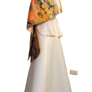 May include: A floor-length white gown featuring a peplum waist and a draped shawl overlay. The shawl is decorated with a detailed pattern of orange and yellow chrysanthemums, gold accents, and a large white crane bird motif on a dark background.
