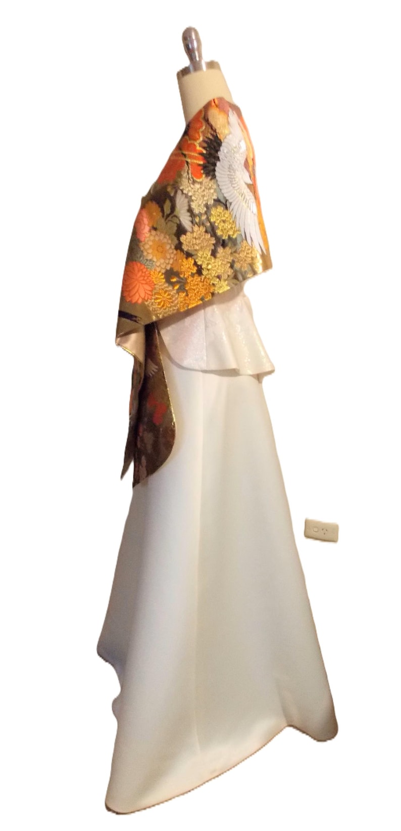 May include: A floor-length white gown featuring a peplum waist and a draped shawl overlay. The shawl is decorated with a detailed pattern of orange and yellow chrysanthemums, gold accents, and a large white crane bird motif on a dark background.