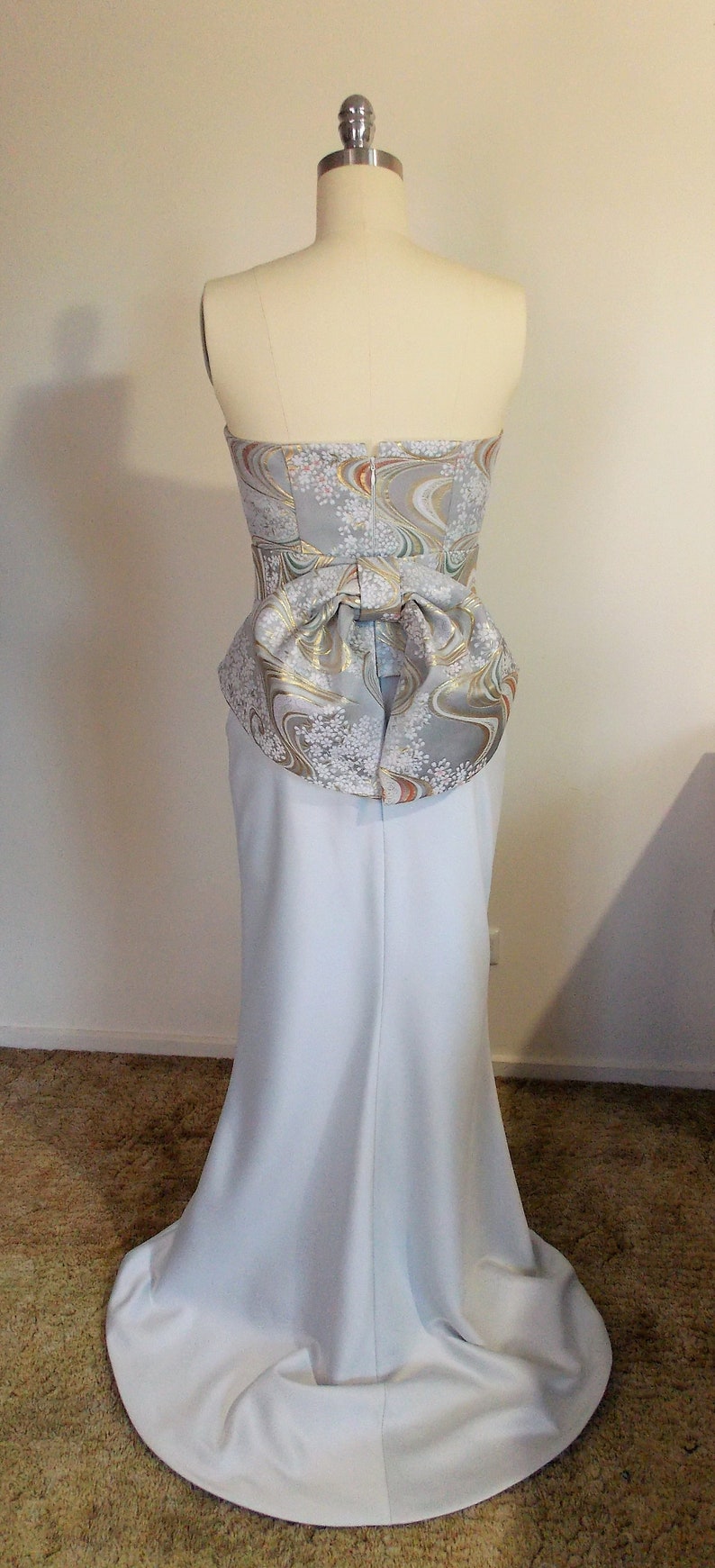 Puede incluir: Un vestido azul claro sin tirantes con un corpi&ntilde;o ajustado y una falda fluida. El corpi&ntilde;o presenta un lazo decorativo hecho de una tela estampada con acentos dorados, blancos y marrones.