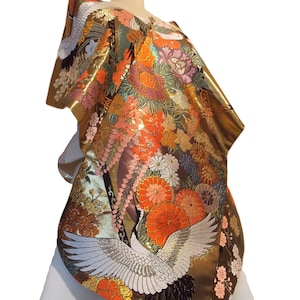May include: A metallic gold kimono featuring intricate embroidery of white cranes with black-tipped wings, surrounded by vibrant orange, pink, and purple floral patterns including chrysanthemums and cherry blossoms on a shimmering fabric base.