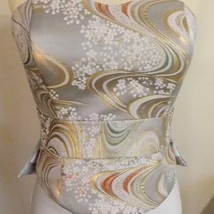 Puede incluir: Un cors&eacute; sin tirantes con un estampado floral plateado, dorado y rojo. El cors&eacute; tiene un corpi&ntilde;o ajustado y una cintura ce&ntilde;ida.