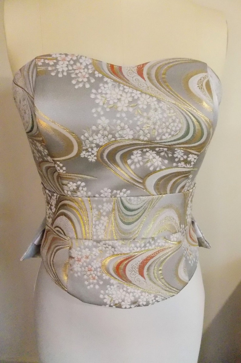 Puede incluir: Un cors&eacute; sin tirantes con un estampado floral plateado, dorado y rojo. El cors&eacute; tiene un corpi&ntilde;o ajustado y una cintura ce&ntilde;ida.