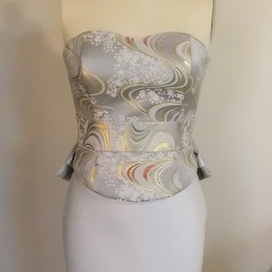 Puede incluir: Un vestido de novia sin tirantes con un corpi&ntilde;o estampado en plata y blanco y una falda fluida.