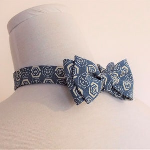 Puede incluir: Una pajarita azul con un patrón geométrico blanco. La pajarita está atada y lista para usar.