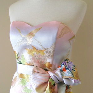 Op de afbeelding: Een witte strapless jurk met een roze en blauwe bloemenprint en een bijpassende band die in een strik om de taille is geknoopt.