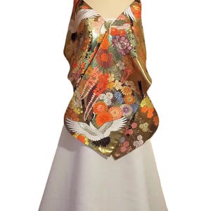 May include: A sleeveless garment featuring a metallic gold bodice adorned with a vibrant, multi-colored floral pattern and white crane motifs. The bodice transitions into a solid, floor-length white skirt with a smooth, flared silhouette.