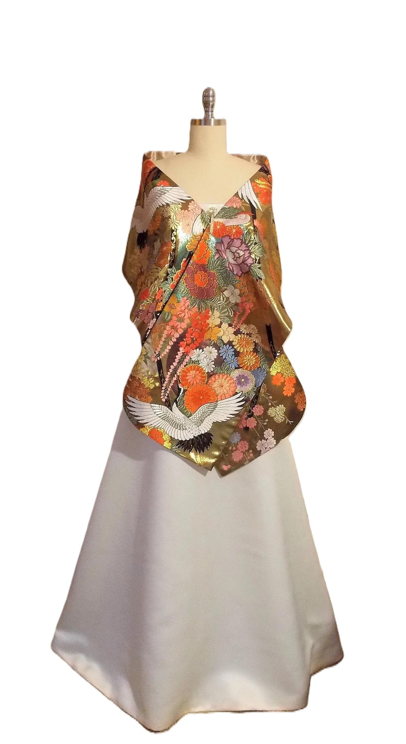 May include: A sleeveless garment featuring a metallic gold bodice adorned with a vibrant, multi-colored floral pattern and white crane motifs. The bodice transitions into a solid, floor-length white skirt with a smooth, flared silhouette.