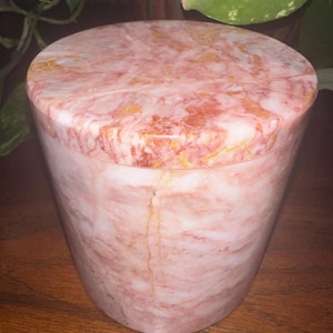 May include: A pink and white marble cylindrical container with a lid. The marble has a swirling pattern with hints of gold.