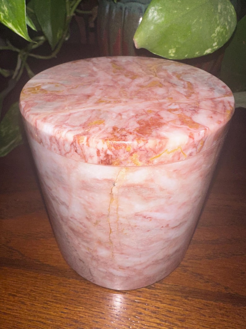 May include: A pink and white marble cylindrical container with a lid. The marble has a swirling pattern with hints of gold.