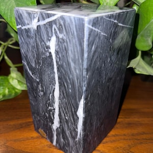 May include: A black and white marble paperweight with a square shape. The marble has a swirling pattern of white veins.