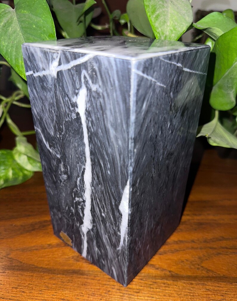 May include: A black and white marble paperweight with a square shape. The marble has a swirling pattern of white veins.