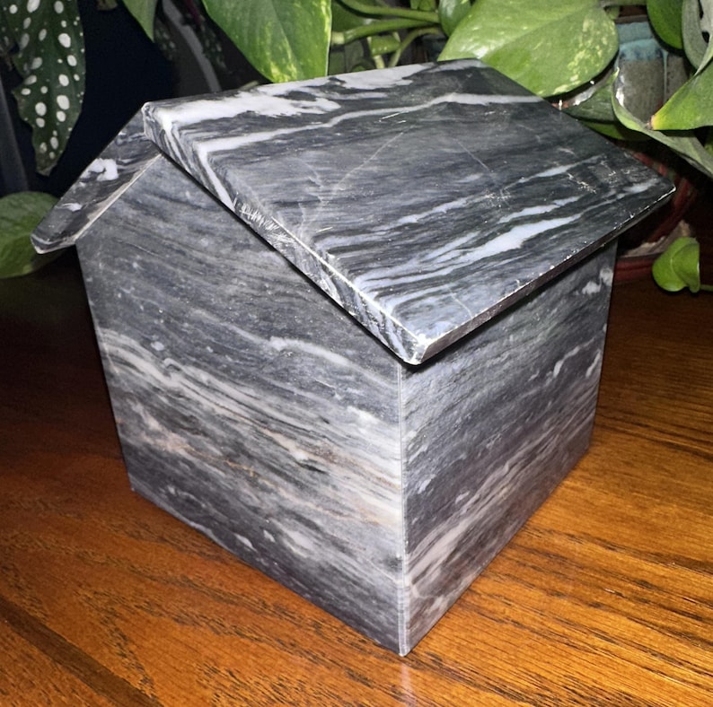 May include: A small, gray and white marble house-shaped box with a hinged lid. The box is made of polished marble with a swirling pattern.