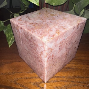 May include: A pink marble cube box with a light pink and white marbled pattern. The box has a smooth, polished surface.