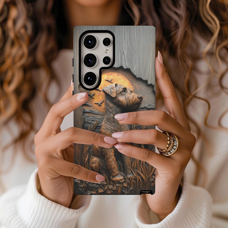 May include: A phone case featuring a detailed illustration of a dog in a field with a sunset and birds. The case has a wooden texture on the top and a black border. The dog is brown and tan, and the sunset is orange.