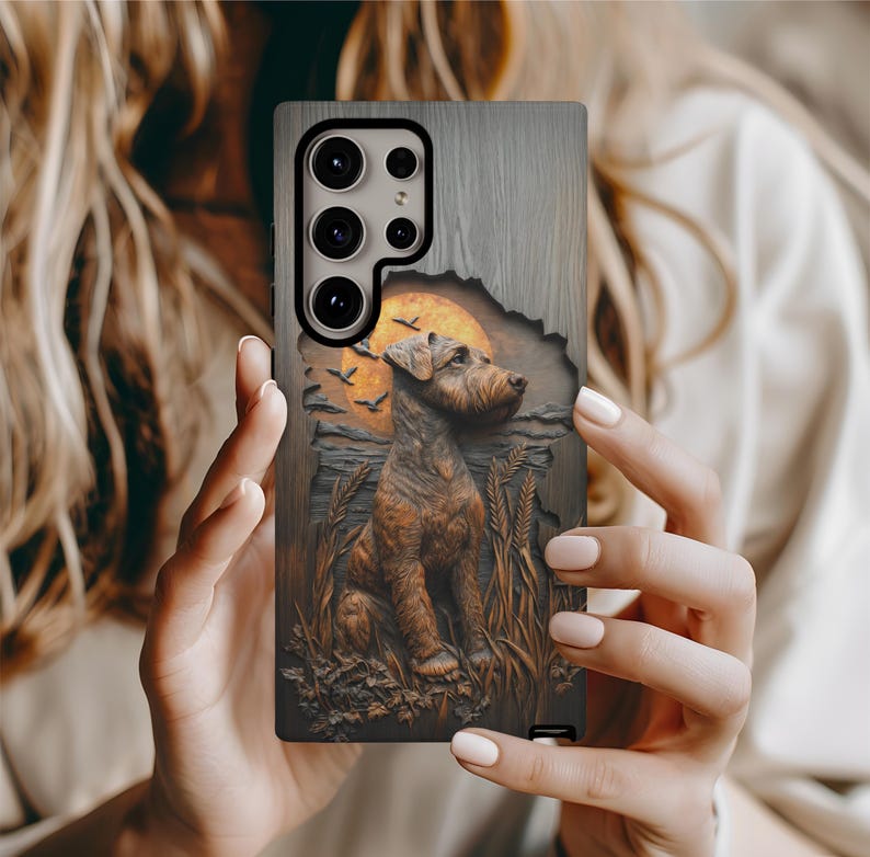 May include: A phone case with a detailed relief of a dog, wheat, and a sunset. The case has a wood-grain texture and a brown and orange color scheme. The dog is the central focus, with a sunset and birds in the background.