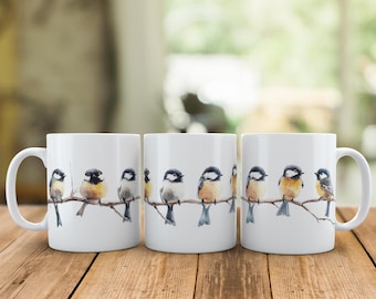 May include: Three white ceramic mugs with a watercolor design of a row of small birds perched on a branch. The birds are black, white, brown, and yellow.