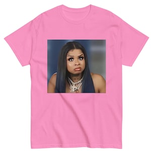 May include: A pink t-shirt with a printed image of a woman with long dark hair and a serious expression. She is wearing a silver necklace with a cross pendant.