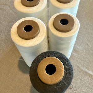 May include: Five spools of thread. Four are white with brown centers, and one is black with a brown center. The spools are cylindrical and appear to be made of tightly wound thread.