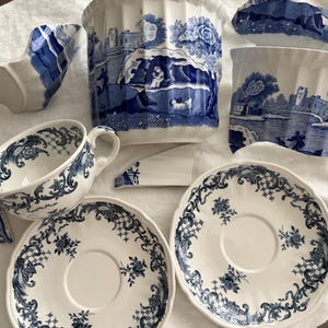 Puede incluir: Una colección de piezas de cerámica rotas con patrones de transferencia en azul y blanco. El conjunto incluye una taza de té, dos platillos y varias secciones fragmentadas de un recipiente acanalado, decoradas con intrincados motivos florales y paisajes.