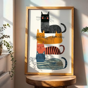 Puede incluir: Una impresión artística enmarcada que presenta una pila de gatos estilizados en negro, naranja, rojo y azul con patrones de rayas. Los gatos tienen diseños simples y minimalistas con los ojos cerrados y largos bigotes. La obra de arte se exhibe en un taburete de madera.